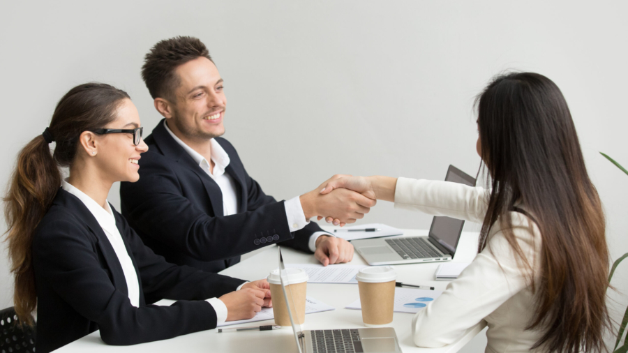 Friendly satisfied partners handshaking at group meeting thanking for successful teamwork, smiling millennial businessman shaking hand greeting businesswoman, respect or making contract deal concept