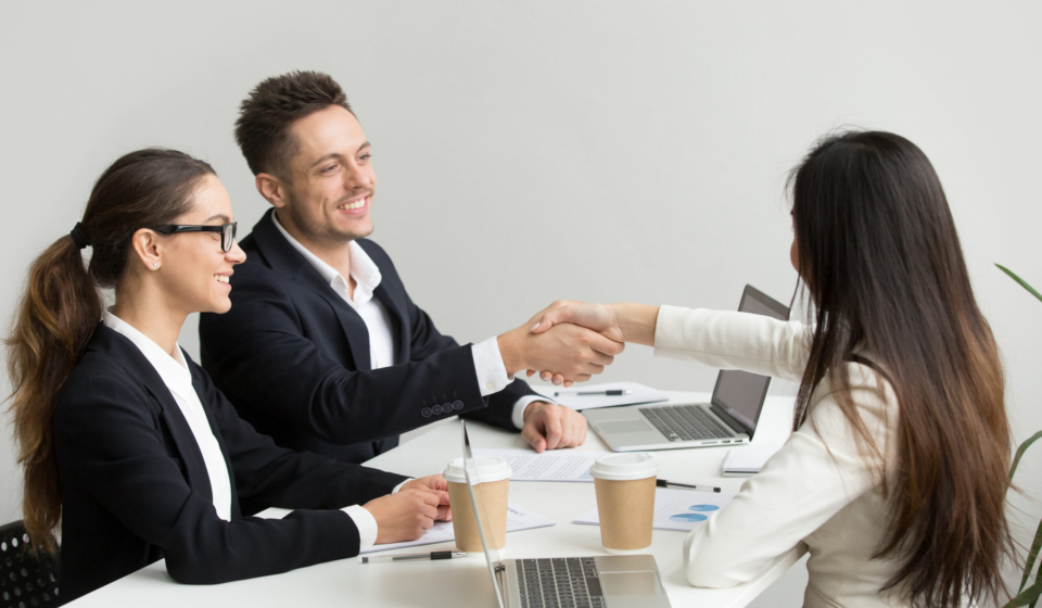 Friendly satisfied partners handshaking at group meeting thanking for successful teamwork, smiling millennial businessman shaking hand greeting businesswoman, respect or making contract deal concept