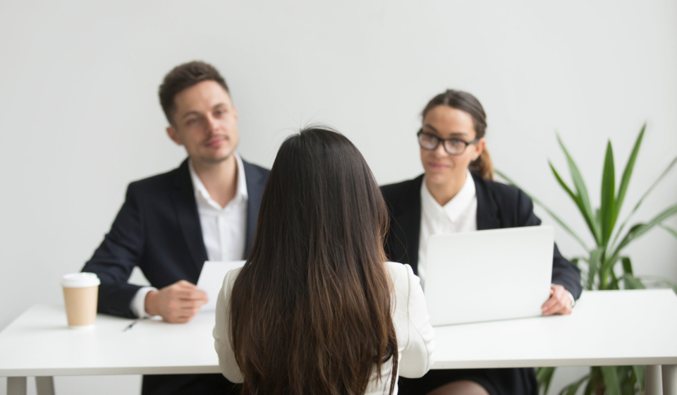 Back close up view of female applicant being interviewed by two HR managers reading her resume, checking data on laptop, asking questions for job position. Employment, hiring, first impression concept